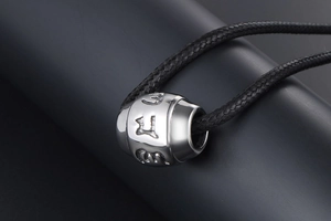 Macro detail of silver titanium steel bead with engraved Six-Word Mantra symbols and black cord