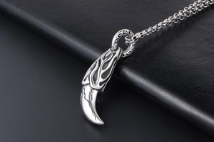 Macro shot of silver-tone wolf tooth pendant with flame relief and metallic chain