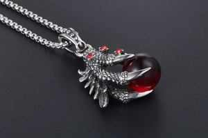 Close-up of a dragon claw pendant holding a red crystal bead on a silver chain necklace
