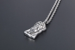 Macro shot of 3D embossed Jesus head pendant in vintage silver steel on black texture