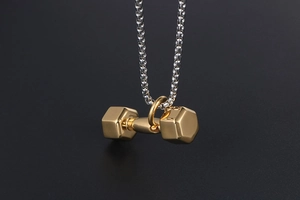 Gros plan d'un pendentif haltère doré sur une chaîne à billes avec un fond texturé sombre