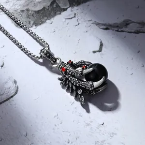 Retro punk dragon claw necklace with black bead and red gemstone eyes on a rocky surface