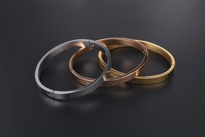Macro detail of brushed titanium steel heart sutra bangles in gold, silver, and rose gold