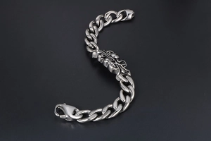 Macro detail of gothic cross plaque on a silver-tone stainless steel Cuban link bracelet