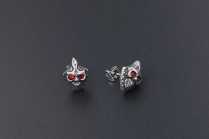 Macro detail of gothic skull stud earrings with red crystal eyes and vintage finish