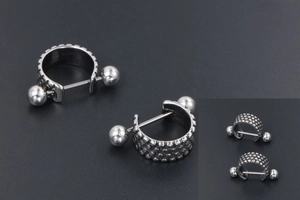 Close-up of silver titanium steel punk earrings with textured dot patterns and barbell studs