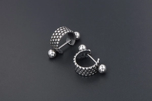 Detail view of titanium steel hoop earrings with industrial polka dot texture and metal bar