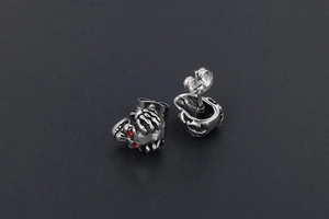 Vue détaillée de boucles d'oreilles tête de mort en acier avec yeux en cristal rouge
