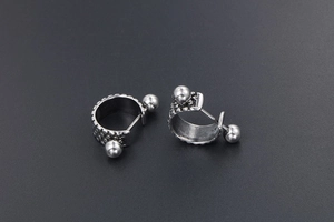 Macro shot of silver titanium steel earrings with woven snake texture and bead detail