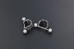 Détail de boucles d'oreilles vintage en acier avec gravures florales et finition argentée