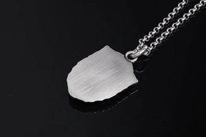 Détail macro du pendentif bouclier militaire argenté avec texture brossée et chaîne rollo