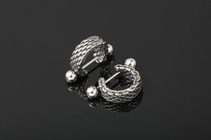 Macro shot of silver hip-hop earrings with braided texture on a reflective black surface