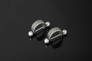 Macro shot of silver barbell piercing featuring triple braided twist and polished steel finish
