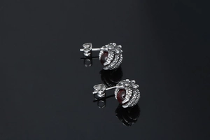 Detail of silver dragon claw earrings holding dark red garnet stones with mirror reflection