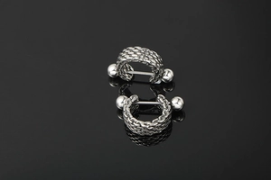 Macro shot of silver titanium steel barbell earrings with intricate woven chain texture