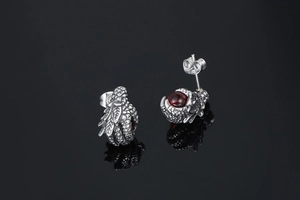 Detailed view of silver dragon claw earrings with round red stones on a black reflective surface