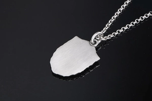 Macro d'un pendentif bouclier argenté montrant la texture du métal brossé et les détails