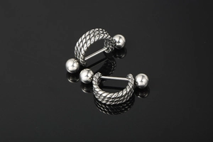 Macro view of punk style stainless steel barbell earrings with twisted rope texture and studs