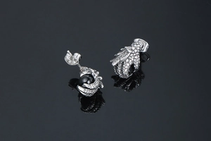 Detailed close-up of 3D dragon claw earrings holding a black bead on reflective surface