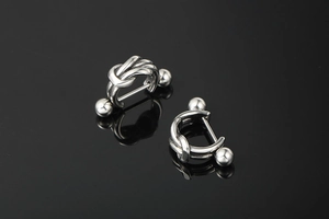 Close-up of silver twist knot hoop earrings with ball ends on reflective black background