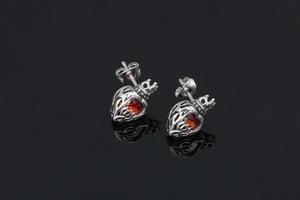 Detailed close-up of crown heart earrings with red stones on a reflective black surface