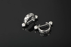 Macro view of silver braided twist barbell earring on a black reflective surface