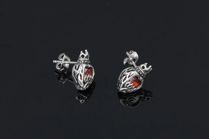 Close-up of heart-shaped crown stud earrings with red stone in vintage silver finish