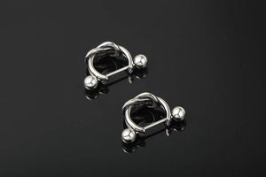 Macro detail of silver titanium knot earrings with ball barbell studs on black background