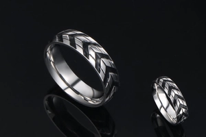 Close-up of titanium steel rings featuring black V-shaped tire tread patterns on black surface