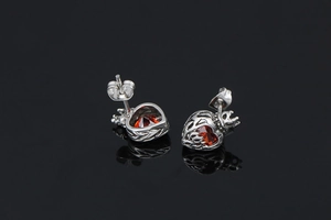 Detailed close-up of heart-shaped ruby earrings with silver crown design on black reflective surface