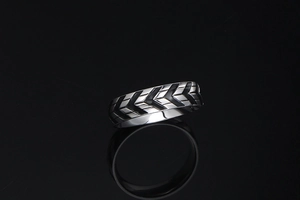 Macro shot of silver titanium ring with black tire tread pattern on black mirror background