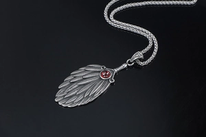 Macro view of vintage feather fan pendant featuring a ruby-red stone and aged metal finish
