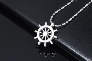 Macro side view of polished silver nautical ship wheel pendant on a beaded chain
