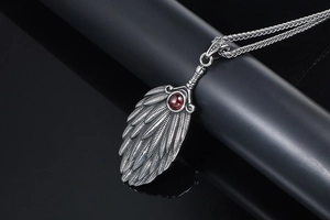 Macro detail of silver feather pendant with red gemstone on black mirror display
