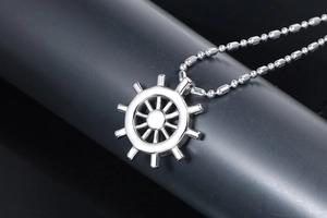 Detailed view of silver stainless steel ship wheel pendant with beaded chain on a stand