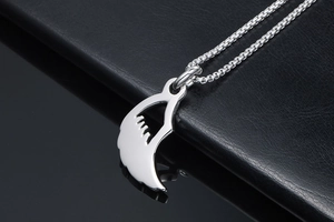 Detail eines polierten Silberflügelanhängers an einer Box-Kette auf schwarzem Leder