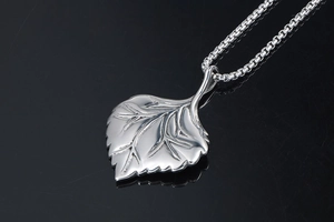 Detailed close-up of a silver leaf pendant with intricate vein texture on a black background