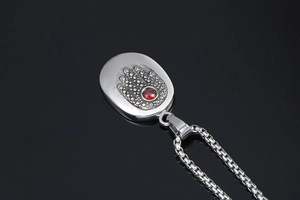 Macro detail of Hamsa Hand pendant with a red gemstone on a silver box chain