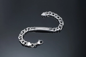Macro shot of silver stainless steel chain bracelet with textured plate on dark mirror