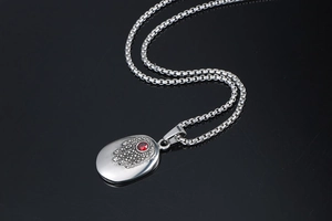 Macro detail of Hamsa Hand engraved pendant with red crystal on a silver steel box chain