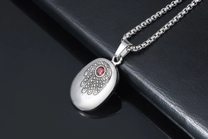 Macro shot of silver Hamsa Hand pendant with a red zircon on a square link chain