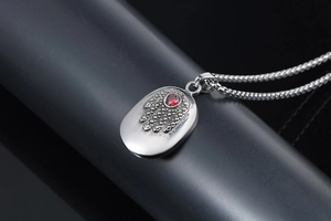 Detailed close-up of a silver Hamsa pendant featuring a red ruby stone on a link chain