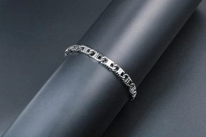 Detailed view of silver chain bracelet with iconic Triomphe links on a black display stand