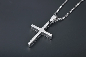Détail d'un pendentif croix en acier titane argenté vintage avec relief et chaîne box