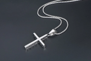 Détail d'un pendentif croix en acier titane argenté avec gaufrage sur chaîne box
