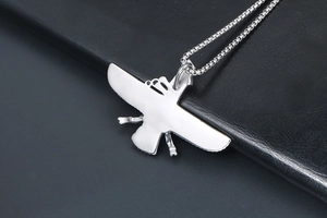 Macro detail of silver eagle pendant with polished finish and box chain on black leather