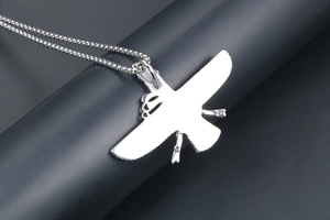 Close-up of a silver-tone flying bird pendant with spread wings on a black stand