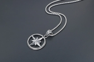 Macro detail of silver compass star pendant with box chain on dark textured surface
