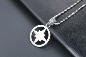 Macro detail of silver compass star pendant with box chain on dark textured background
