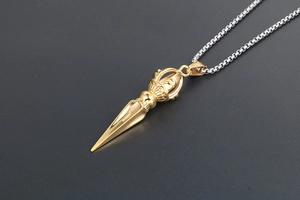 Detailed close-up of a gold-plated Vajra pestle pendant with intricate Buddhist carvings